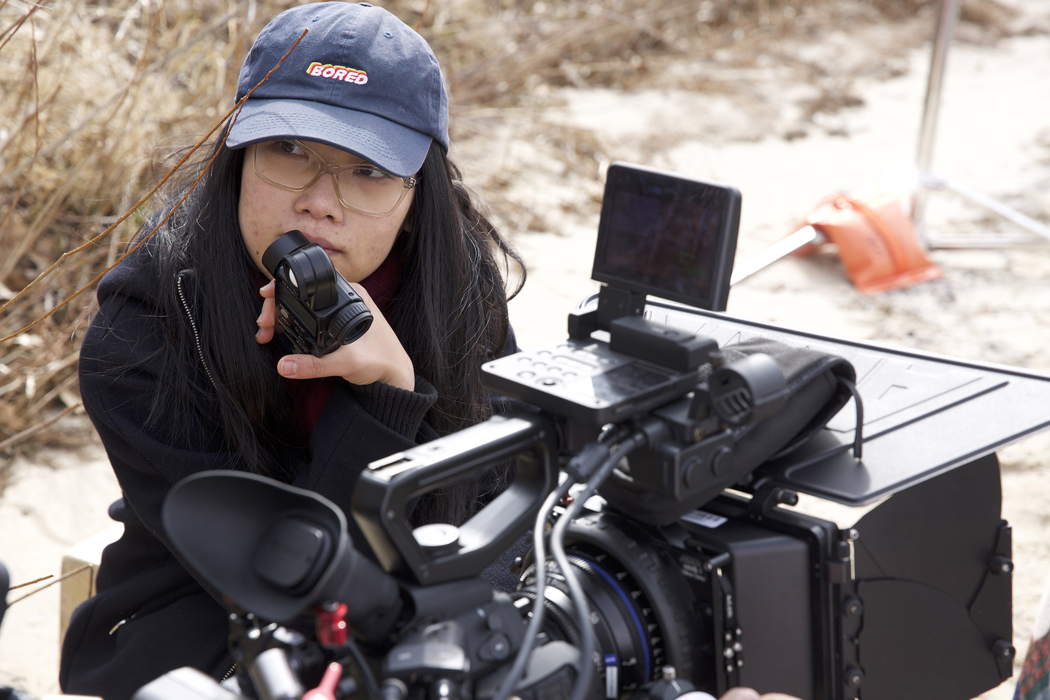 A student looking off screen as she adjusts the settings of a film camera. 